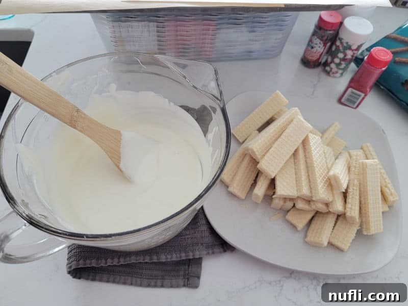 Melted white candy bark in a glass bowl next to vanilla wafers and holiday sprinkles, ready for dipping
