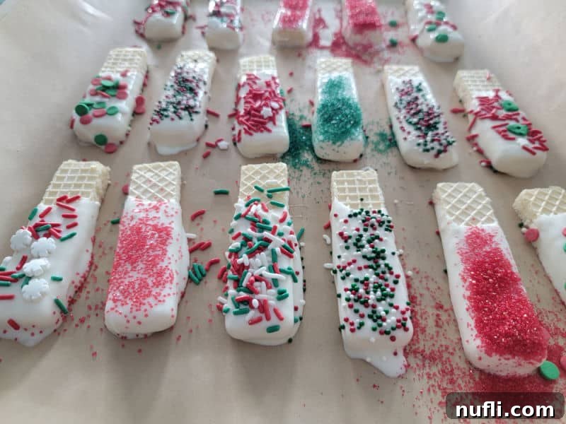 A chocolate-dipped wafer cookie is lavishly coated with a colorful assortment of holiday sprinkles, ready to set.