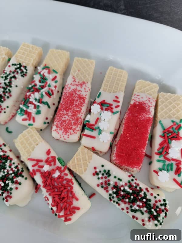 A close-up shot of white chocolate-dipped wafer cookies, generously coated with a festive mix of holiday sprinkles.