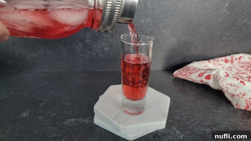 Crimson Capture 7 Cocktail shaker pouring into a shot glass on a white coaster next to a red and white cloth napkin