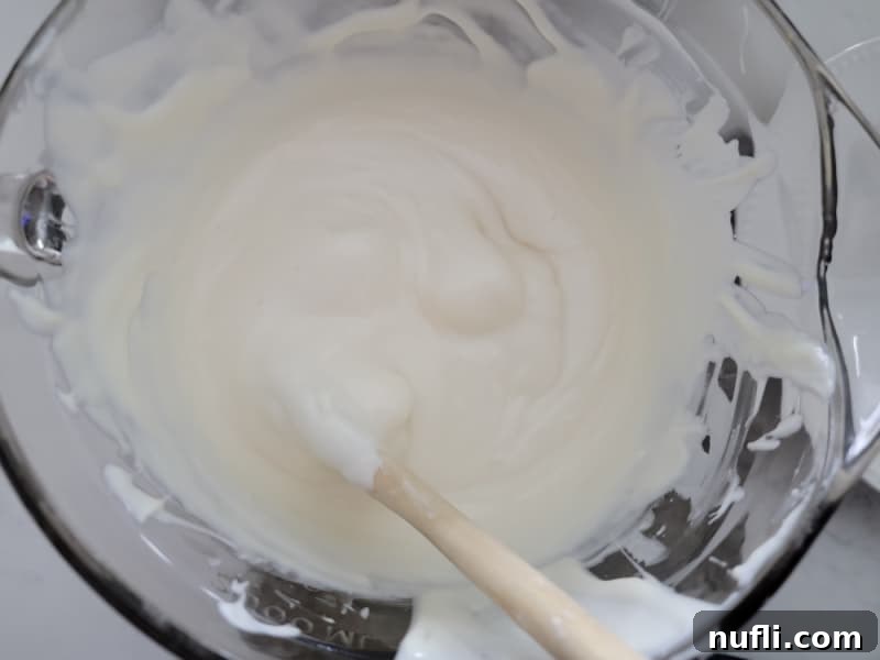 Crispy Chocolate Dream Bites 4 Melted vanilla almond bark in a clear glass bowl with a wooden spoon for chocolate covered rice krispie treats.