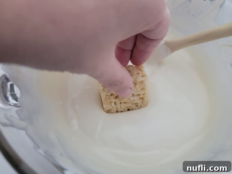Crispy Chocolate Dream Bites 5 Rice Krispie treat dipping into a bowl of almond bark for Chocolate covered rice krispie treats