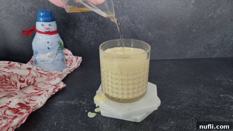 Bourbon pouring into a glass filled with eggnog for a bourbon eggnog cocktail