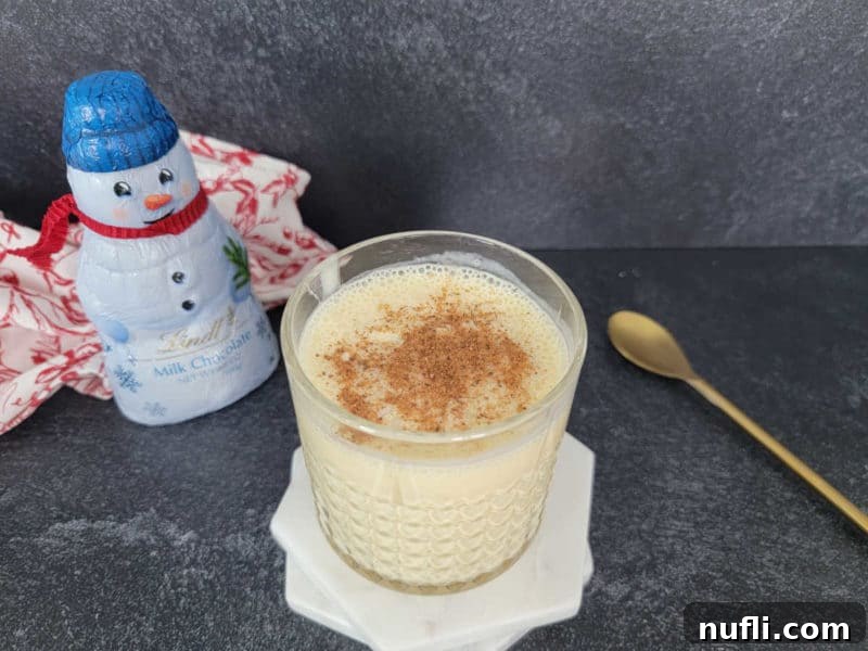 Bourbon Eggnog cocktail in a glass next to a snowman chocolate and gold spoon