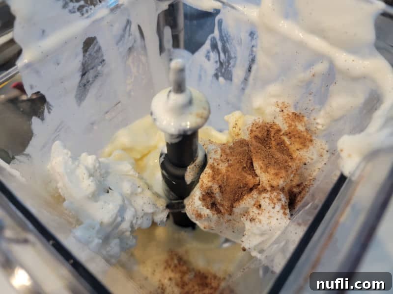 Eggnog Shake ingredients, including eggnog, vanilla ice cream, and nutmeg, prepared in a blender before blending.