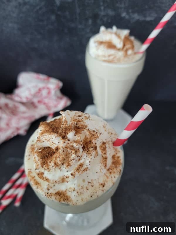 A festive Eggnog shake in a milkshake glass, elegantly garnished with a swirl of whipped cream and a sprinkle of ground nutmeg, ready to be enjoyed with a red striped straw.