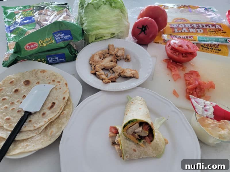 Chicken wrap on a white plate next to chicken, tortillas, diced tomatoes, and mayo