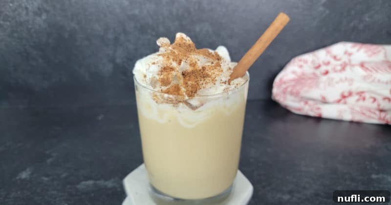 Decadent Eggnog Mudslide 11 Eggnog Mudslide Cocktail elegantly topped with whipped cream, a sprinkle of ground nutmeg, and a festive cinnamon stick for garnish. The drink is in a clear glass.