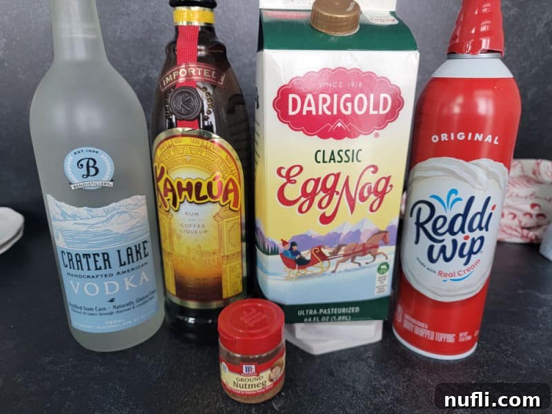 Decadent Eggnog Mudslide 3 Ingredients for an Eggnog Mudslide laid out: a bottle of vodka, a bottle of Kahlúa, a carton of eggnog, a bowl of whipped cream, and a small bowl of ground nutmeg.