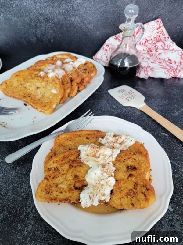 Effortless Eggnog French Toast 9 Eggnog French Toast slices on a white plate garnished with eggnog whipped cream and cinnamon/nutmeg next to a platter and a spatula