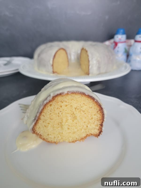 Slice of Eggnog cake covered in eggnog glaze on a white plate