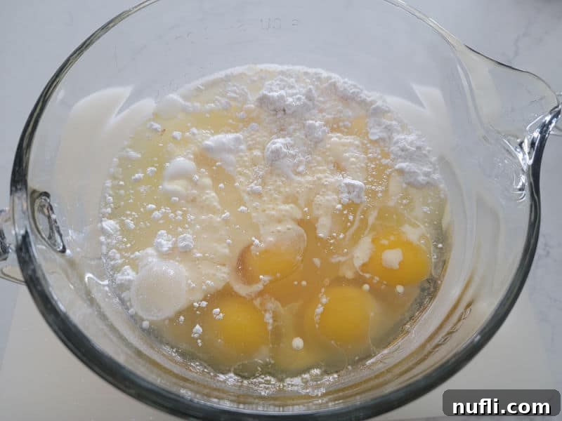 Vanilla cake mix in a glass bowl with eggs before mixing for eggnog cake