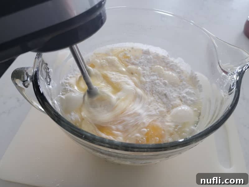 Hand mixer mixing eggnog cake ingredients in a glass bowl