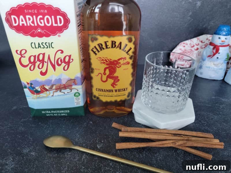 A high-angle shot showcasing a classic eggnog glass filled with a cinnamon stick, a bottle of Fireball Cinnamon Whisky, and a gold spoon, set against a cozy backdrop.