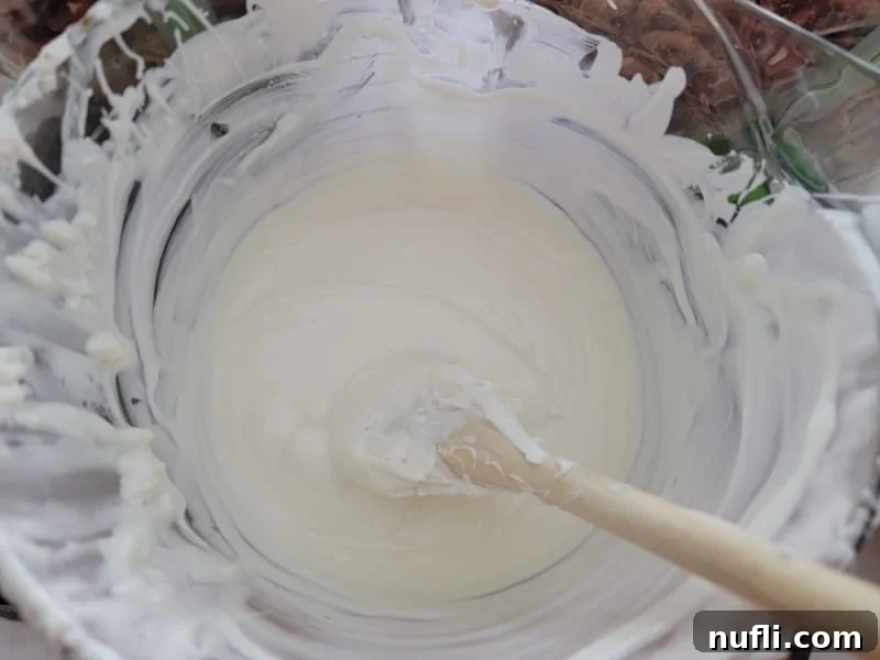 White almond bark melted in a glass bowl with a wooden spoon for Reindeer Muddy Buddies