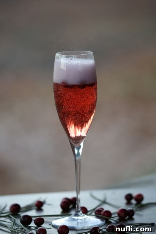 A close-up of a sparkling Cranberry Mimosa in a champagne flute, vibrant red and full of delicate bubbles, ready to be enjoyed.