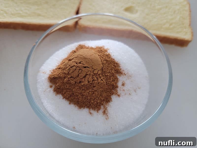 Cinnamon on top of sugar in a glass bowl near bread. 
