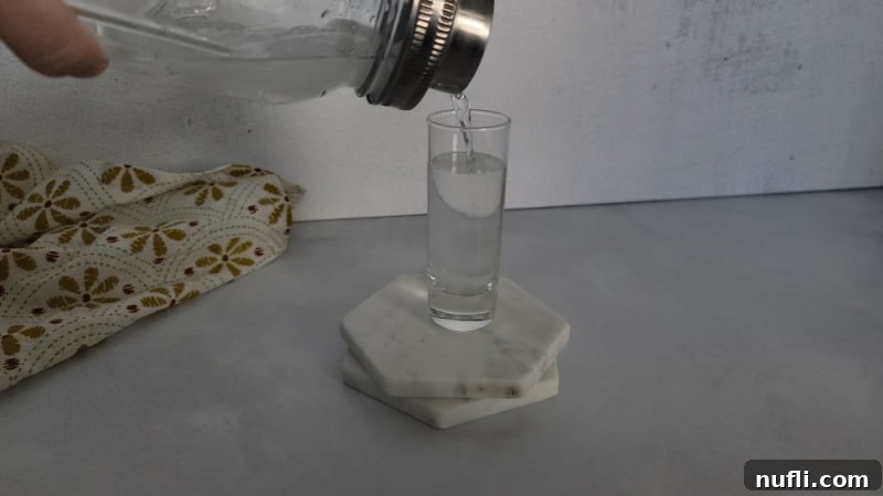mason jar cocktail shaker pouring clear liquid into a shot glass on two coasters