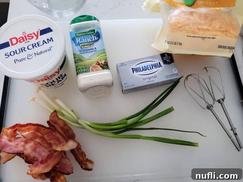 Fresh ingredients laid out for Bacon Cheddar Ranch Dip: sour cream, ranch dressing mix, cream cheese, crispy bacon slices, shredded cheddar cheese, and vibrant green onions.