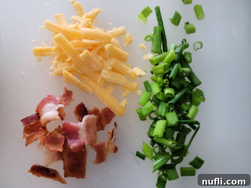 A colorful array of chopped green onions, crispy bacon bits, and shredded cheddar cheese on a cutting board, prepared as garnishes for the dip.