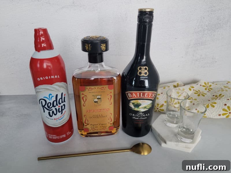 Mastering the Blowjob Shot 3 Whipped cream, amaretto, Baileys Irish cream, two shot glasses on a coaster, and a gold bartender's spoon laid out for making the shot.