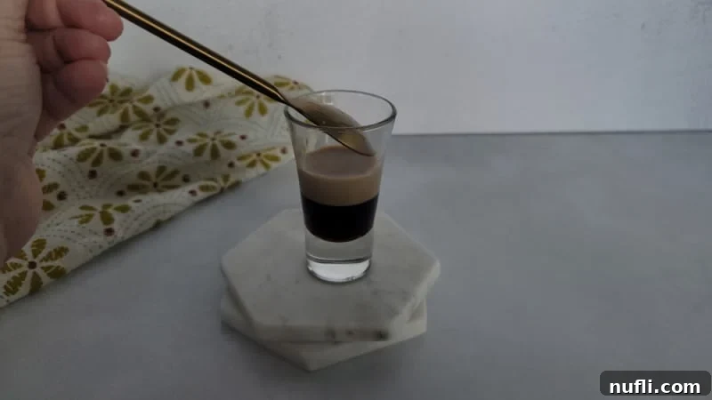 Mastering the Blowjob Shot 5 Long bar spoon in a shot glass with two distinct layers of liquid, demonstrating the layering technique.