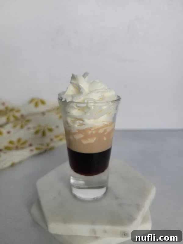 Mastering the Blowjob Shot 6 Whipped cream perfectly dolloped on a layered Blowjob Shot, sitting on two white marble coasters.