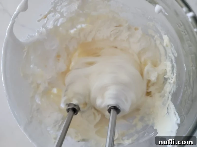 Mixer beaters whipping cream cheese in a glass bowl for Marshmallow Fruit Dip