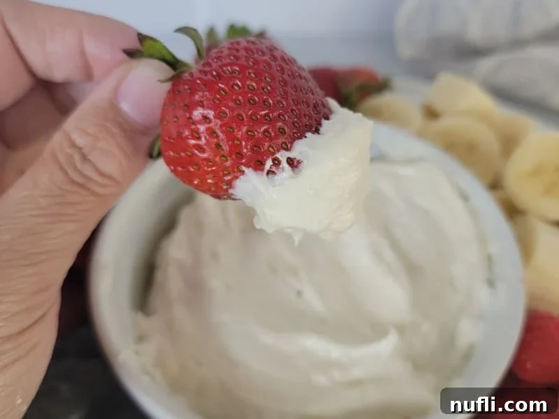 Strawberry covered in marshmallow fruit dip above a white bowl filled with fruit dip