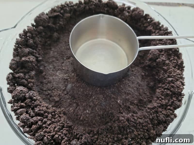 Easy Oreo Pie Crust 6 measuring cup pressing an Oreo Crust into a pie dish