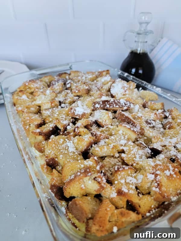 A wide shot of the baked Overnight French Toast breakfast casserole in a glass baking dish, with a jar of maple syrup nearby, inviting diners to indulge.