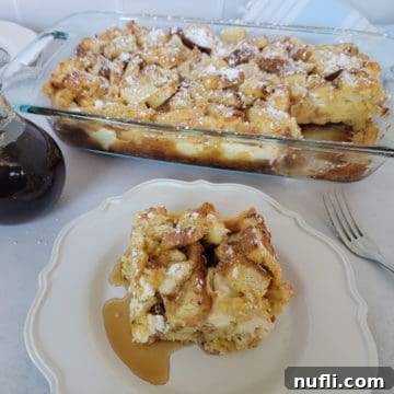 Square of golden Overnight French Toast Casserole on a white plate in front of a full casserole dish.