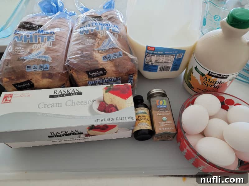 Arrangement of fresh ingredients for Overnight French Toast Casserole including sliced bread, cream cheese, milk, maple syrup, vanilla extract, ground cinnamon, and eggs on a rustic cutting board.