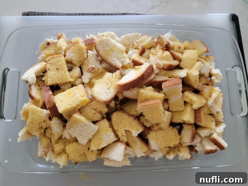 The egg mixture poured over cubed bread in a casserole dish, thoroughly soaking the bread for an overnight French Toast casserole breakfast.