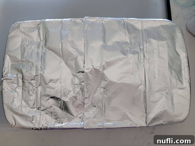 A casserole dish, now covered with aluminum foil, indicating it's ready for baking after overnight refrigeration.