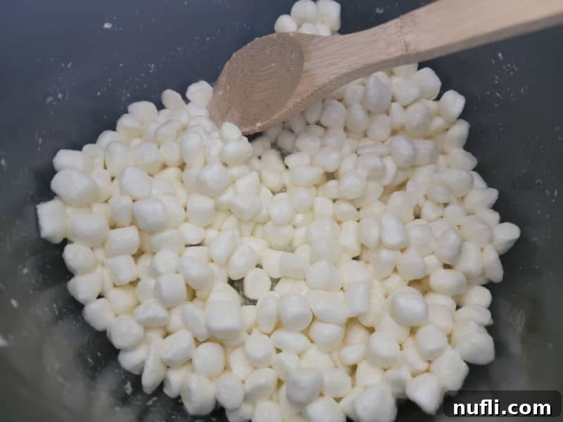 Mini Marshmallows in a dark pot with a wooden spoon for Rice Krispie Treats
