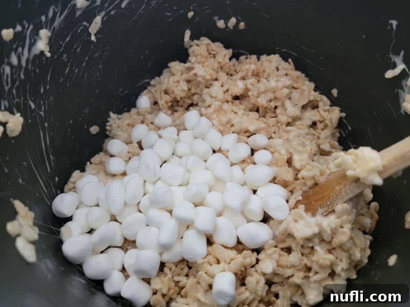 Mini marshmallows on rice krispie cereal in a dark pot for Rice Krispie treats. 