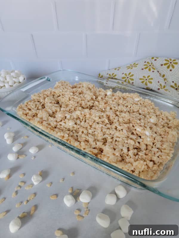 Glass casserole dish filled with the best Rice Krispie Treats surrounded by mini marshmallows and rice cereal on a white counter