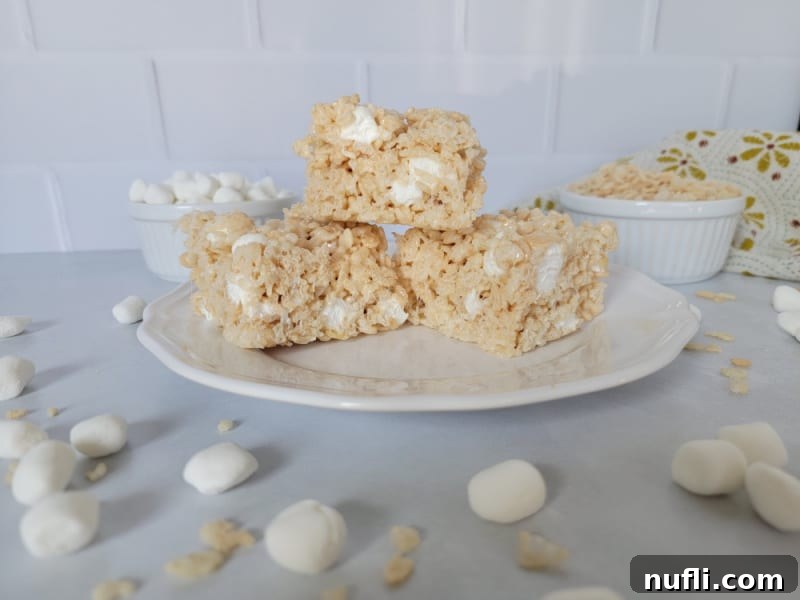 Gooey Rice Krispie Treats stacked on a white plate with mini marshmallows surrounding the plate