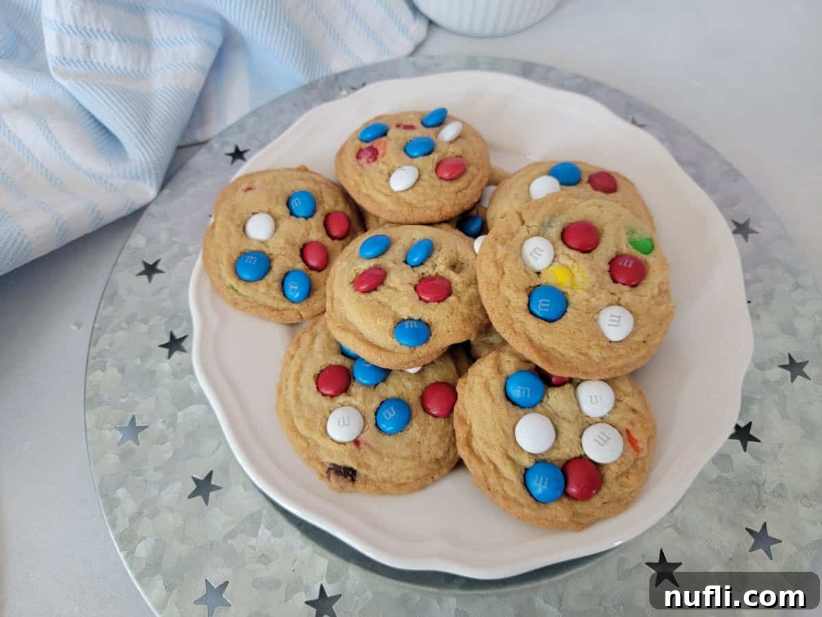 Red, White, and Blue M&M cookies on a white plate on a silver platter, next to a cloth napkin, perfect for patriotic holidays.