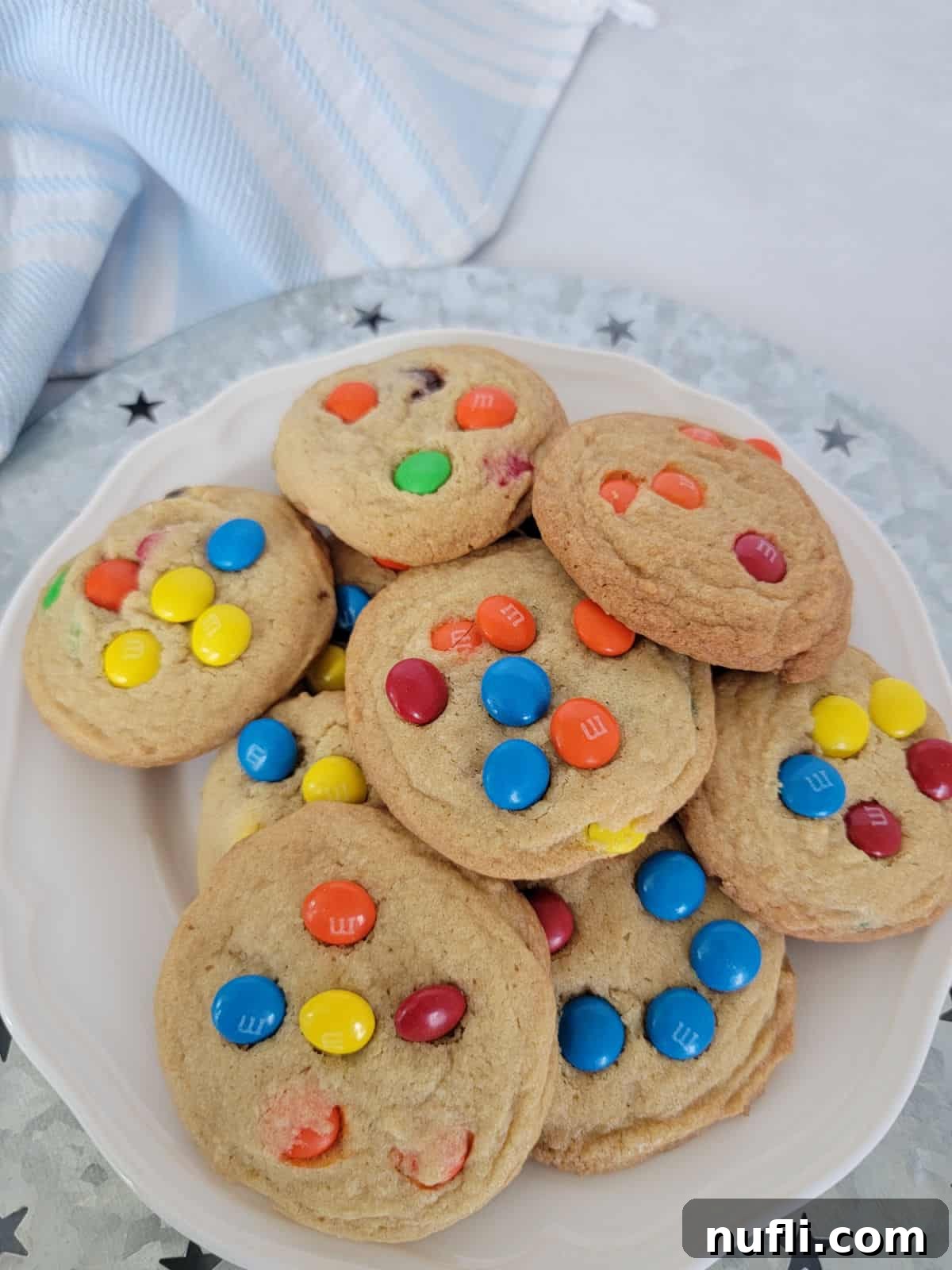 M&M Cookies on a white plate on a silver platter next to a cloth napkin, ready to be served.