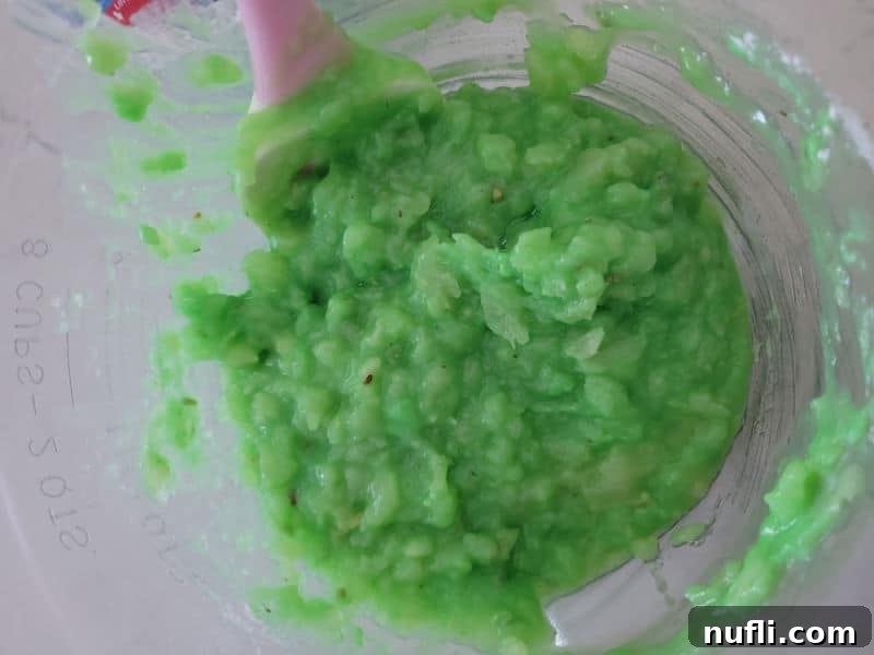 Pineapple and pistachio pudding mixed together in a glass bowl with a spatula for Watergate Salad. 