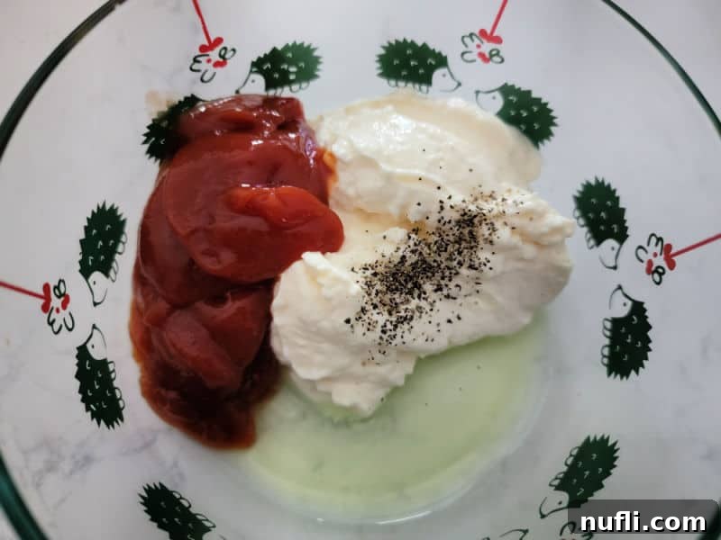 Fry sauce ingredients (mayonnaise, ketchup, pickle juice, black pepper) in a glass bowl before mixing