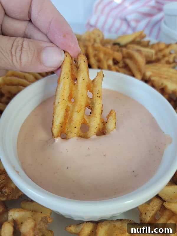 Close-up of a crispy waffle fry being dipped into a bowl of creamy Fry Sauce