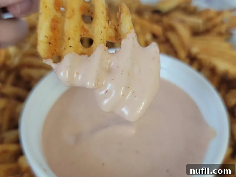 A crispy waffle fry delicately dipping into a white bowl filled with creamy Fry Sauce