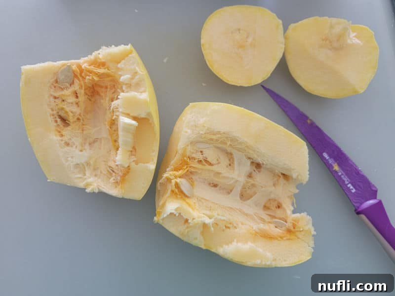 Easy Air Fryer Spaghetti Squash 4 A spaghetti squash carefully sliced in half lengthwise, revealing its inner cavity, positioned beside a purple-handled knife on a clean cutting board.