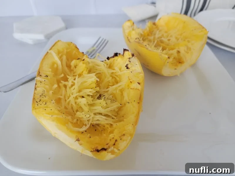 Easy Air Fryer Spaghetti Squash 8 A perfectly cooked air fryer spaghetti squash, scraped into tender strands, sits invitingly on a white plate next to a fork, ready to be enjoyed.
