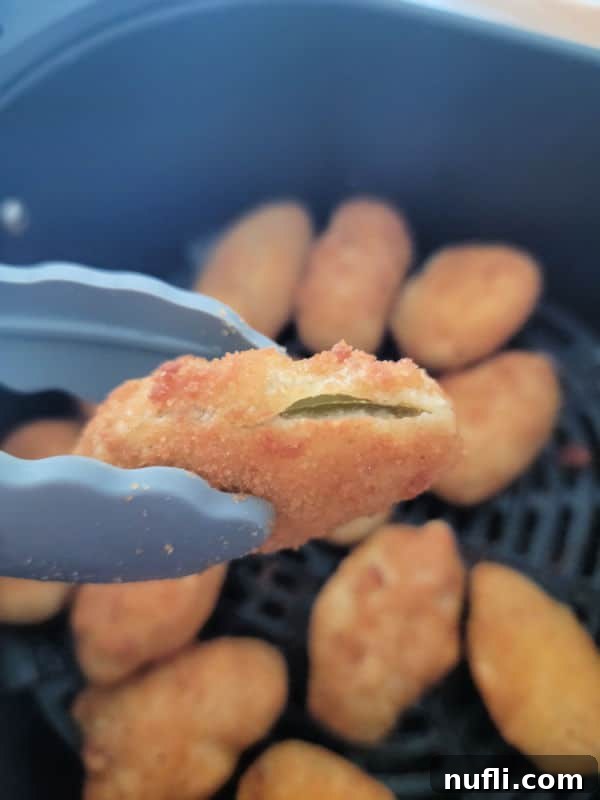 Crispy Air Fryer Frozen Jalapeno Poppers 5 Air fried jalapeno poppers being removed from the air fryer basket with tongs.