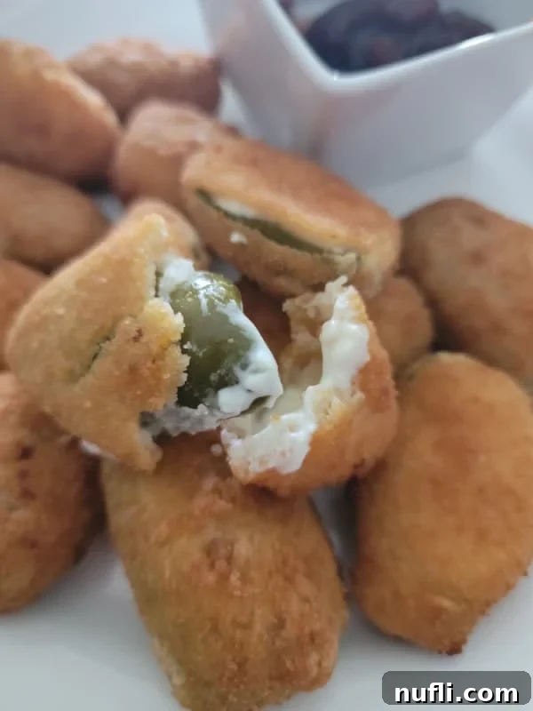 Crispy Air Fryer Frozen Jalapeno Poppers 6 A plate of freshly air-fried jalapeno poppers, one cut open to show the creamy filling.