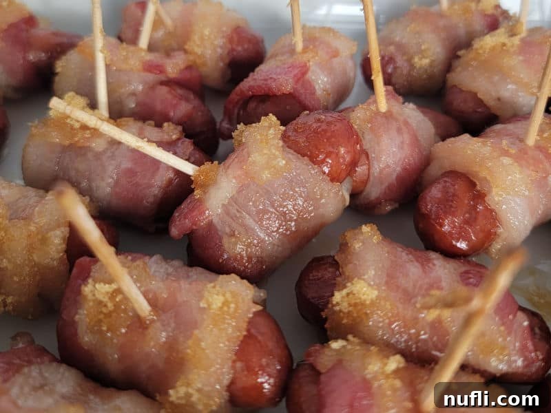 A serving platter filled with baked brown sugar bacon wrapped little smokies, each skewered with a toothpick, ready for guests.